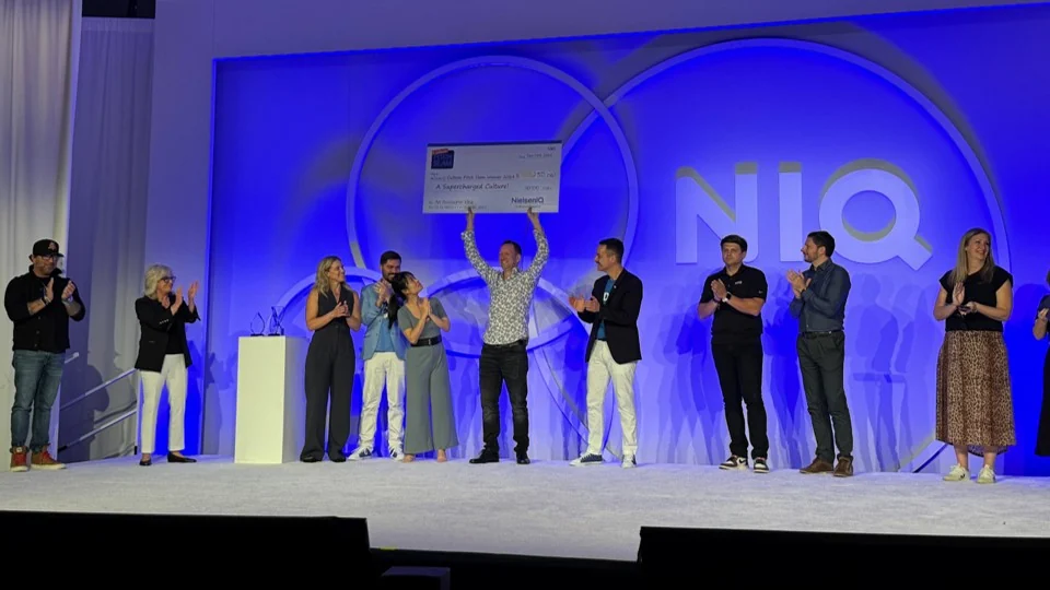 Damian Gayler holding the $250,000 Culture Slam winner's cheque on stage with NIQ colleagues